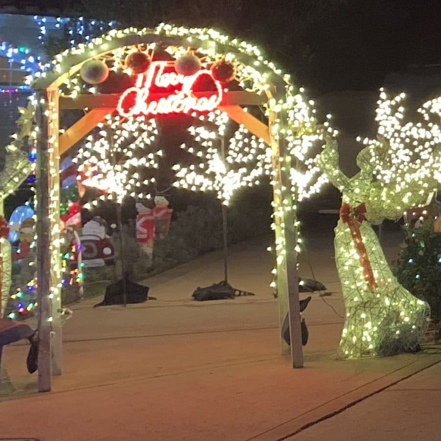 A wooden arch wrapped in warm white lights with a red Merry Christmas sign, next to a light-up reindeer.